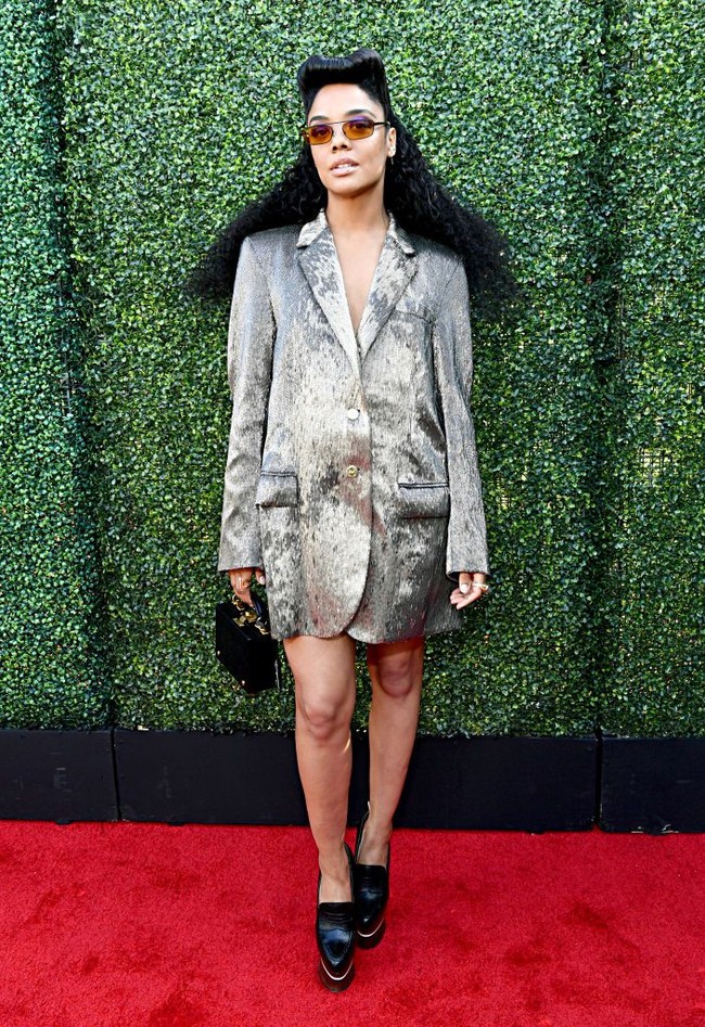 Tessa Thompson lalu menyempurnakan gayanya dengan kacamata hitam dan tas mungil berbentuk boks kecil. (Foto: Getty Images)