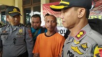 Tampak Hamdani yang menggunakan baju tahanan diapit dua polisi.