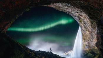 Sebuah gua yang terletak di Pantai Selatan Islandia seolah membingkai cahaya auroa yang memesona yang dipadukan dengan air terjun dengan ratusan bintang-bintang bersinar. Karya ini diabadikan oleh fotografer Sutie Yang. (Foto: Astronomy Photographer 2019)