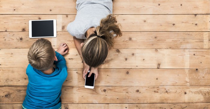 Top view image of two kids lying on the floor and playing with tablet and smartphone watching movie or gaming. Mockup or template for web or application design.