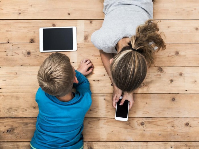 Top view image of two kids lying on the floor and playing with tablet and smartphone watching movie or gaming. Mockup or template for web or application design.