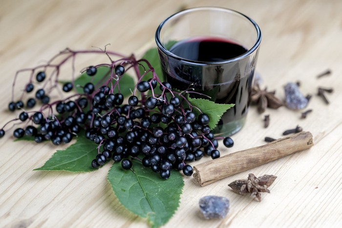 Glass of fresh elderberry syrup with cinnamon stick, brown sugar, star anise and elderberries on a wooden kitchen counter