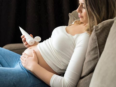 Pregnant woman applying moisturizer cream on her belly.
