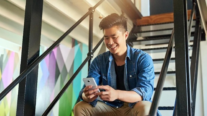 Handsome Korean white collar worker using modern smartphone while spending working day at spacious office