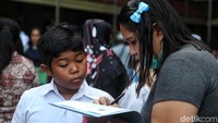 Seorang siswa melihat ibunya mengisi formulir pendaftaran.