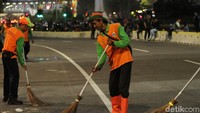 Pasukan Oranye membersihkan sampah dengan menggunakan sapu dan alat-alat kebersihan mereka.