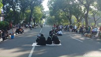 Selain duduk-duduk di trotoar, ada juga yang tampak duduk beralaskan tikar di tengah jalan. Hari ini, Jl Medan Merdeka Barat memang ditutup di dua arah. (Farih/detikcom)