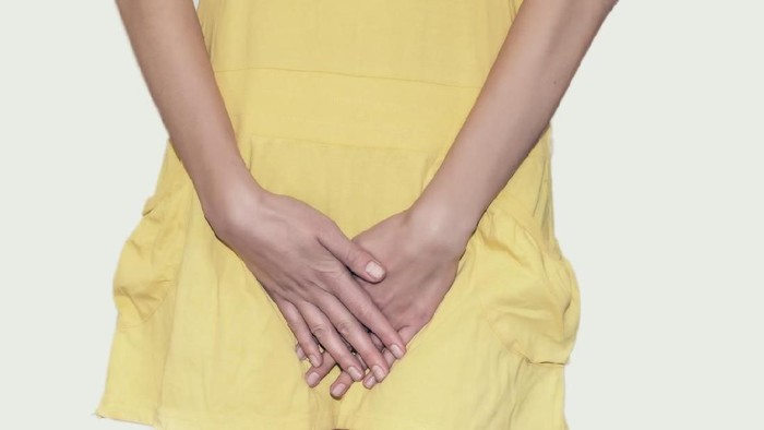 Young woman in yellow short dress standing with her hands between legs, needs a restroom, isolated for white background. Womens health, gynecology.