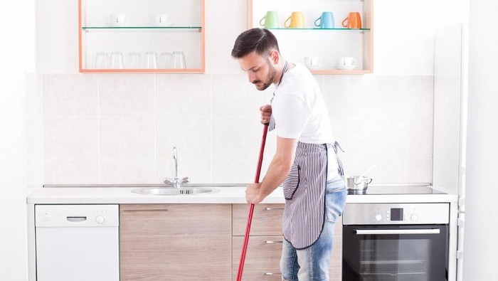 Young handsome man mopping tiled floor in kitchen. Husband housework concept