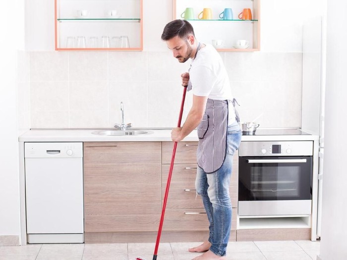 Young handsome man mopping tiled floor in kitchen. Husband housework concept