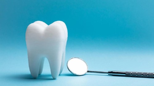 Close-up Of Tooth With Dental Mirror Over Blue Background