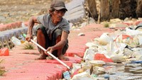 Seorang warga mengumpulkan sampah yang menyebar di sekitar Sungai Ciliwung.