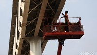 Dua pekerja melakukan pengecatan tiang skybridge.