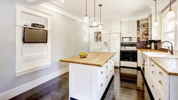 Kitchen interior in white tones with hardwood counter tops, kitchen island and black tile back splash trim. White coffered ceiling with pendant lights make room more elegant.