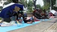 Mereka duduk beralaskan tikar dan terpal, beberapa di antaranya membuka payung untuk menghalau panas.