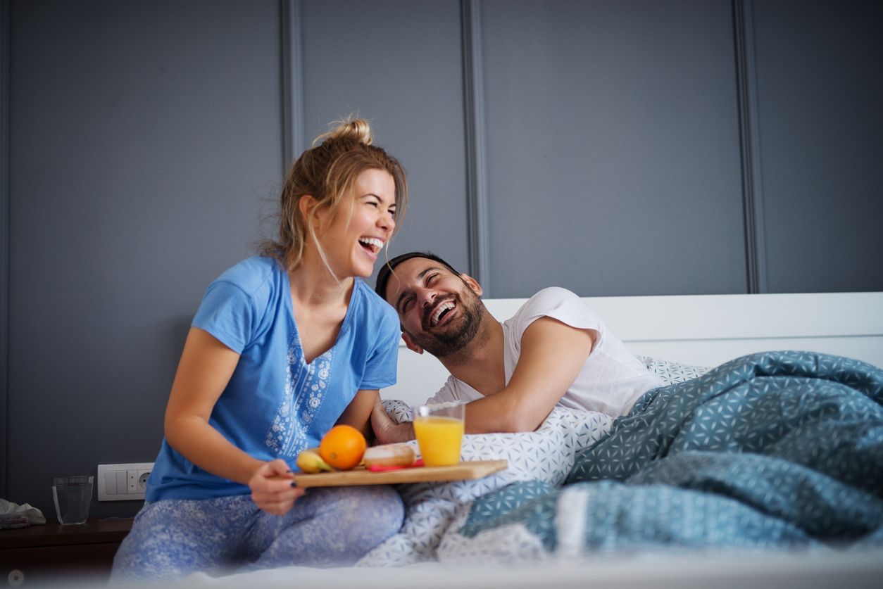 Beautiful happy young romantic girl brings breakfast to her husband in the bed and laughing together after he wakes up.