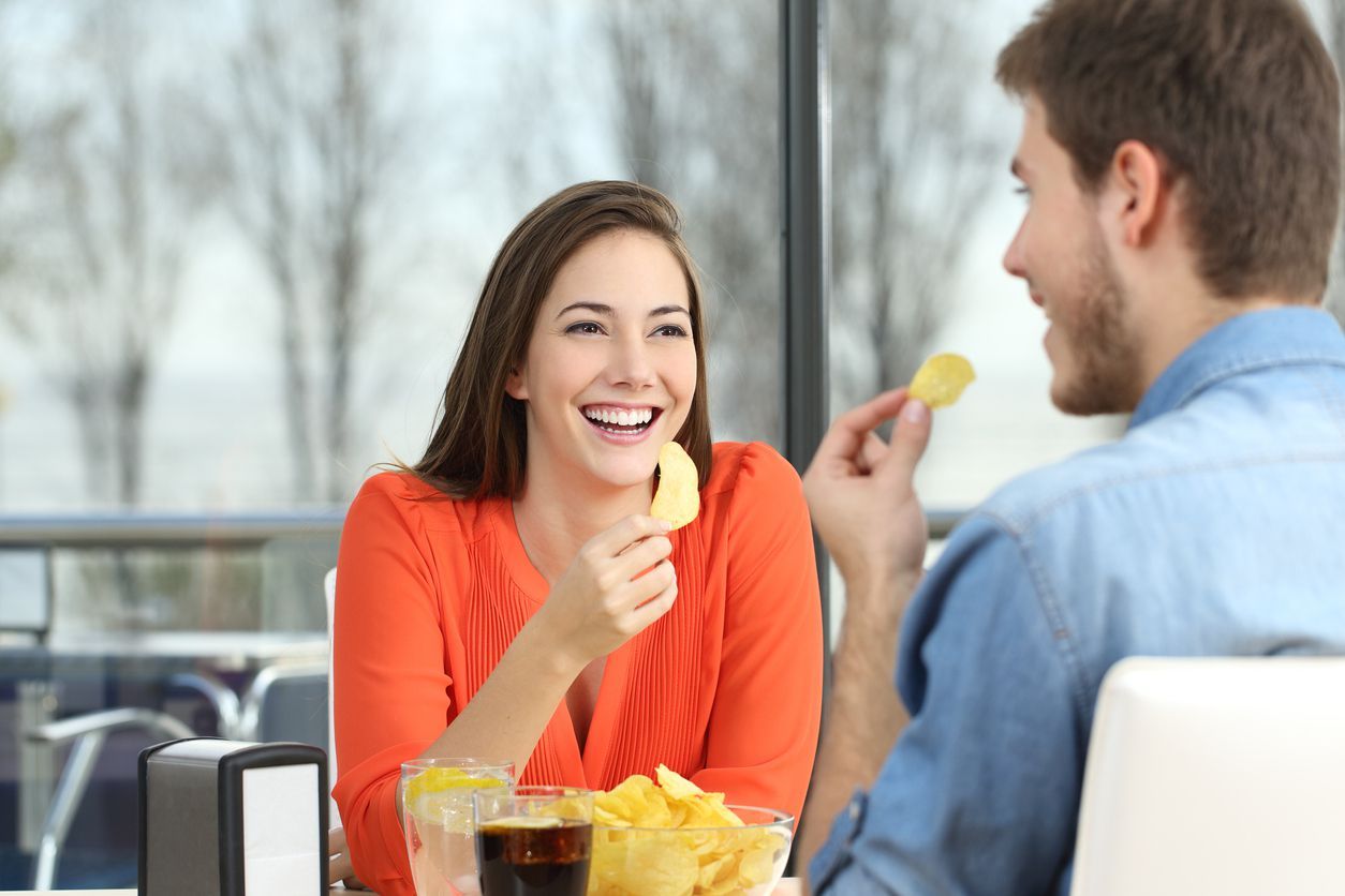 Affectionate couple sitting in the outdoor restaurant in the evening, beautiful blonde woman eating tomato soup.