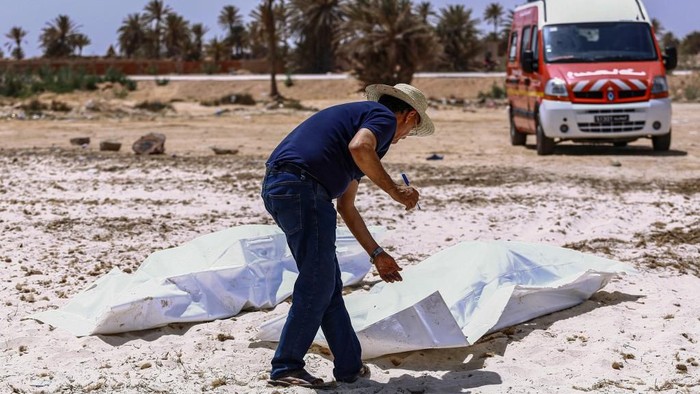 EDITORS NOTE: Graphic content / A representative of the Tunisian Red Crescent association checks bodies recovered from a boat carrying 86 migrants that capsized off the Tunisian coast while crossing the Mediterranean from Libya to Italy, as they lie on a beach in Aghir in Tunisias southern island of Djerba on July 6, 2019. - The latest tragedy came to light the same week as 44 migrants were killed in an air strike on their detention centre in a suburb of the Libyan capital. (Photo by ANIS MILI / AFP)