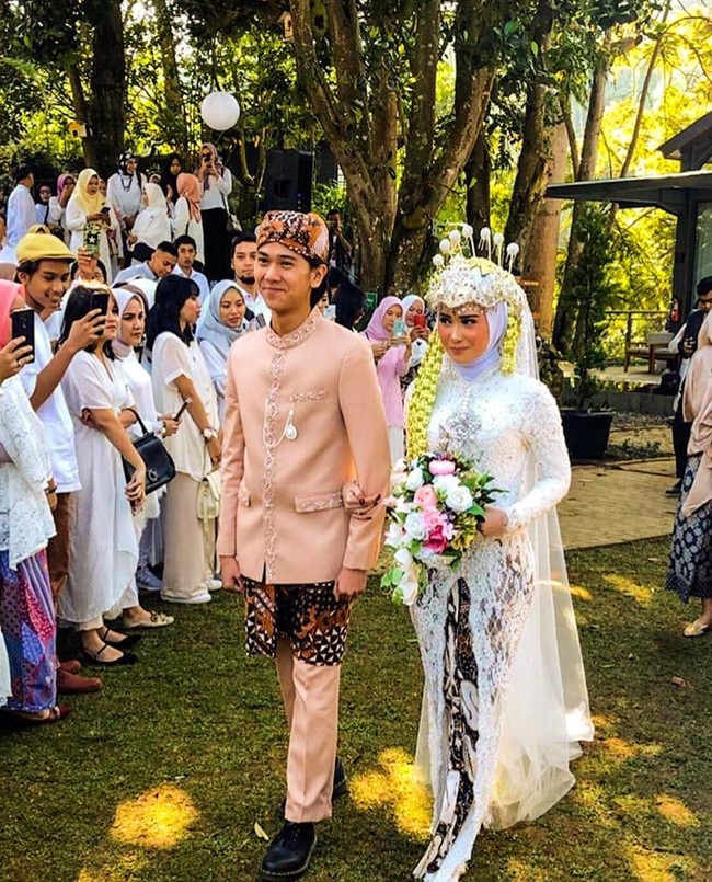 Kebaya pengantin putih yang panjangnya hingga hampir menyapu lantai menjadi pilihan Fildza Hasnamudhia untuk akad nikah. Sentuhan glamour terlihat pada penerapan veil yang panjangnya hingga menyapu lantai. Foto: Instagram @iqbaal.e, Instagram @danikadaviscamakeup