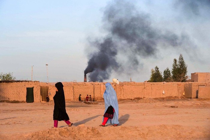 In this photograph taken on April 3, 2019, Afghan women walk near a brick factory as smoke rises up in the sky from a chimney on the outskirts of Jalalabad. (Photo by NOORULLAH SHIRZADA / AFP)