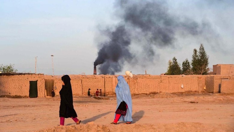 In this photograph taken on April 3, 2019, Afghan women walk near a brick factory as smoke rises up in the sky from a chimney on the outskirts of Jalalabad. (Photo by NOORULLAH SHIRZADA / AFP)