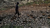 Warga melintas di tanah pinggir sungai yang retak-retak akibat kekeringan.