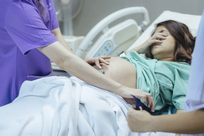 874118774 Doctor examining belly of expectant mother in hospital room. Thailand.
