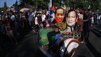 Dua orang warga Solo yang memakai topeng Joko Widodo dan Prabowo Subianto naik becak bersama di acara car free day di Solo, Minggu (14/7/2019).