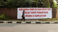 Seorang warga melintas di depan spanduk bertuliskan Kami Warga Komplek Daan Mogot Baru Menolak Tempat Penampungan Imigran di Komplek Kami.