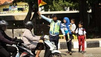 Seorang petugas membantu warga menyeberang jalan usai JPO Jembatan Gantung dibongkar dan kini masih dalam tahap pembangunan.