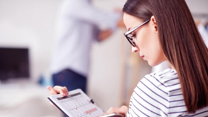Keep the pace of time. Pleasant beautiful concentrated woman holding calendar and cell phone while being involved in work