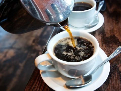 Fresh hot coffee being poured into a cup from a stainless steel french press in a trendy cafe