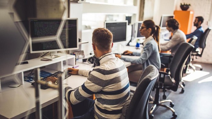 Group of programmers developing new software on desktop PCs in the office. Focus is on man in the foreground.