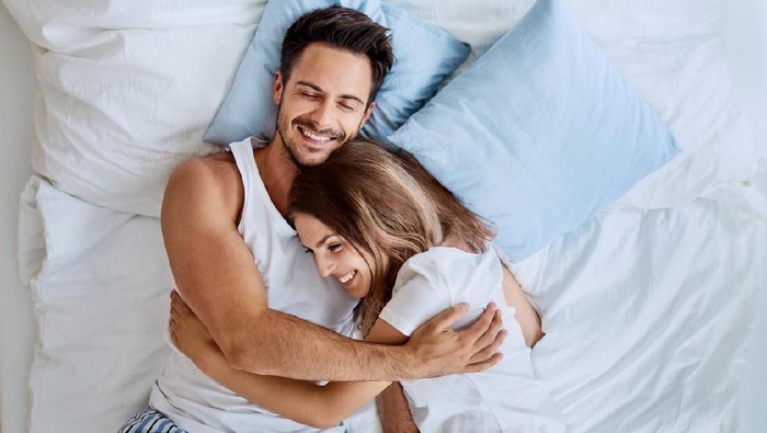 996097632 Top view of beautiful happy young couple lying on bed and hugging