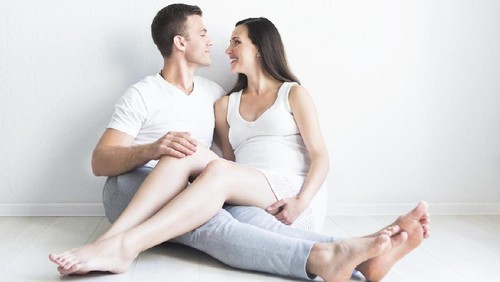 Young man and pretty pregnant woman hugging together indoors