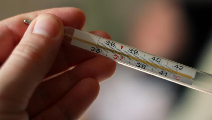 An alcohol thermometer shows a temperature of 37.9 on a blurred background of a sick girl lying on a bed. Check the temperature. Fever, illness, chills, care.