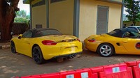 Ada mobil Porsche warna kuning yang juga terparkir. Mobil ini tanpa pelat nomor dengan kondisi kotor.  