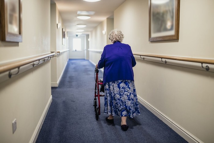 Ilustrasi Nenek 107 Tahun A senior woman walking down a corridor with the assistance of a walker. view from rear