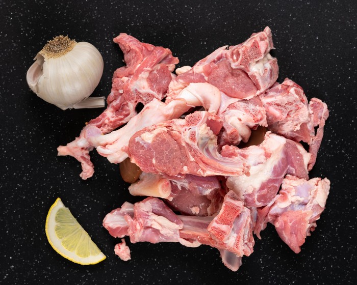 Fresh raw goat meat stew like cuts on black cutting board with  garlic and lemon.