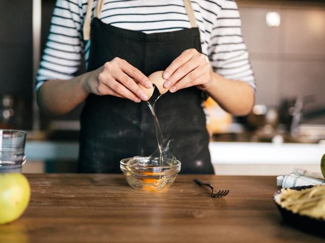 Female hands holding cracked egg over a white bowl