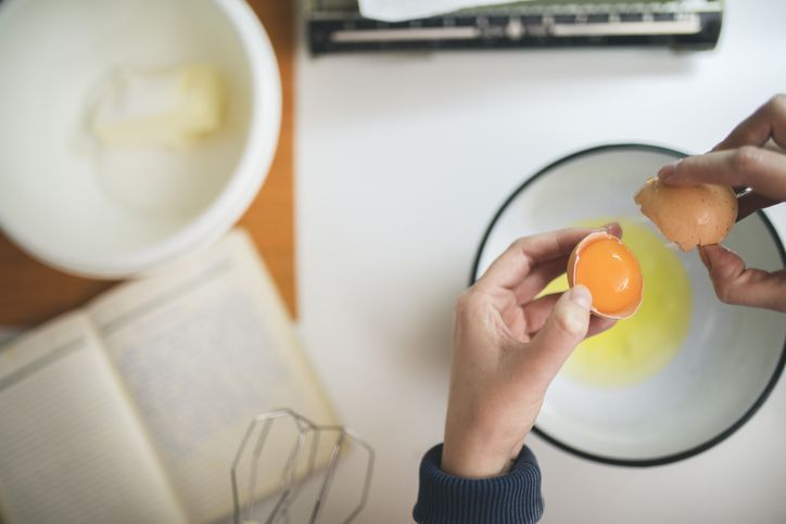 Female hands holding cracked egg over a white bowl