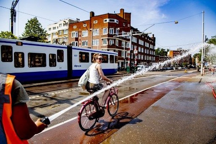 A firefighter sprays water as a woman rides her bicycle on the Wiegbrug bridge, during a heatwave in Amsterdam on July 25, 2019. - On July 24 and 25, 2019, as Europe is hit by a second heatwave in less than a month, Germany, Belgium and The Netherlands top their previous heat records. The Royal Netherlands Meteorological Institute (KNMI) has issued an official warning due to the heat, advising residents of the capital city to stay inside. (Photo by Robin UTRECHT / ANP / AFP) / Netherlands OUT