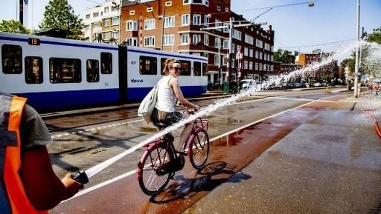 Ilustrasi gelombang panas di Belanda A firefighter sprays water as a woman rides her bicycle on the Wiegbrug bridge, during a heatwave in Amsterdam on July 25, 2019. - On July 24 and 25, 2019, as Europe is hit by a second heatwave in less than a month, Germany, Belgium and The Netherlands top their previous heat records. The Royal Netherlands Meteorological Institute (KNMI) has issued an official warning due to the heat, advising residents of the capital city to stay inside. (Photo by Robin UTRECHT / ANP / AFP) / Netherlands OUT