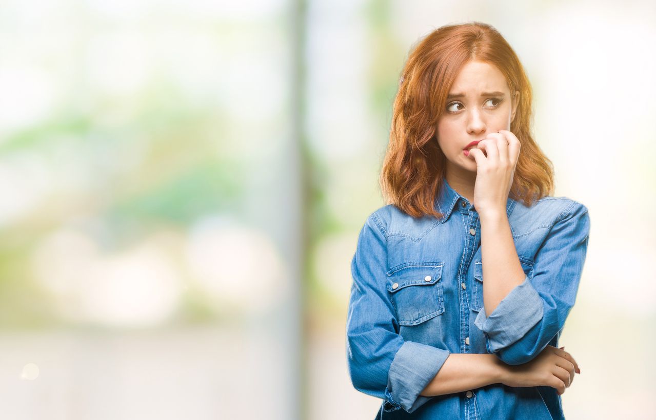 Young beautiful woman over isolated background looking stressed and nervous with hands on mouth biting nails. Anxiety problem.