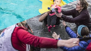 Relawan membantu seorang pria dan bayi pengungsi ketika para pengungsi saat tiba di pantai Pulau Lesbos Yunani setelah melintasi laut Aegea. Foto: Uğur Gallenkuş