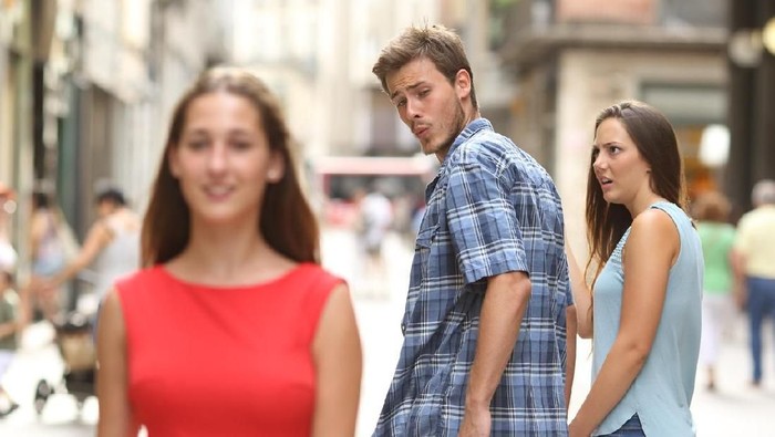 Disloyal man walking with his girlfriend and looking amazed at another seductive girl