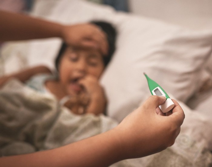 Shot of a little girl lying in bed while her mother takes her temperature with a thermometer