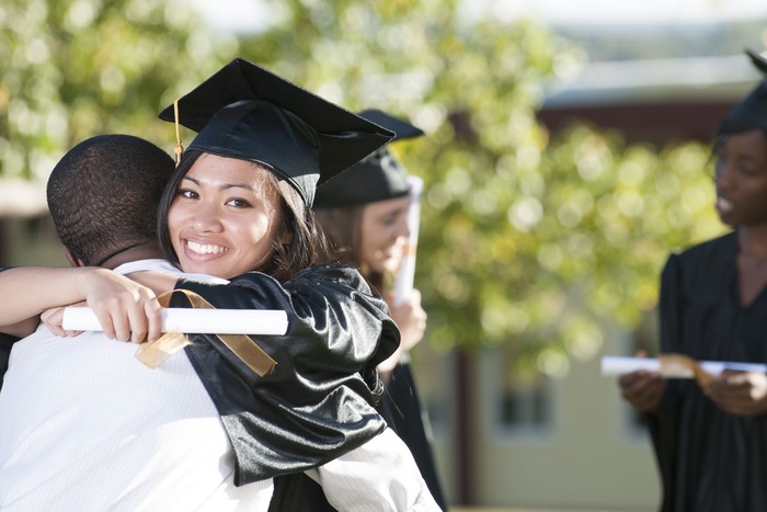 A happy graduate is hugging her friend after their graduation ceremony. She is smiling while looking at the camera.