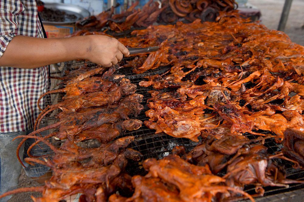 This photo taken on August 10, 2019 shows a man grilling rats at a stall in Battambang province. - Barbecued field rats are not everybody's idea of a tasty treat, but in Cambodia's rural Battambang province they are popular as a cheap - and quick - snack, with small skewered ones going for 0.25USD each while larger rodents can cost 1.25USD. (Photo by TANG CHHIN Sothy / AFP)
