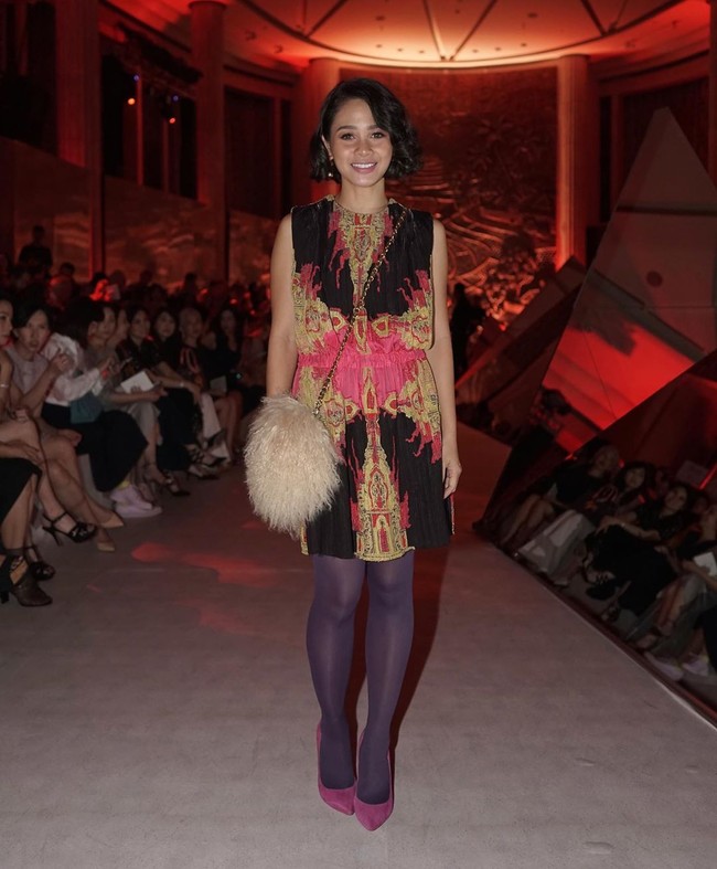 Andien mencuri perhatian dengan polychromatic plissé mini dress dari koleksi Fall/Winter 2019 Sapto. Gaun tersebut disandingkan dengan stocking dan heels berwarna ungu mencolok, berikut tas penuh bulu. Foto: Instagram/@saptodjojokartiko